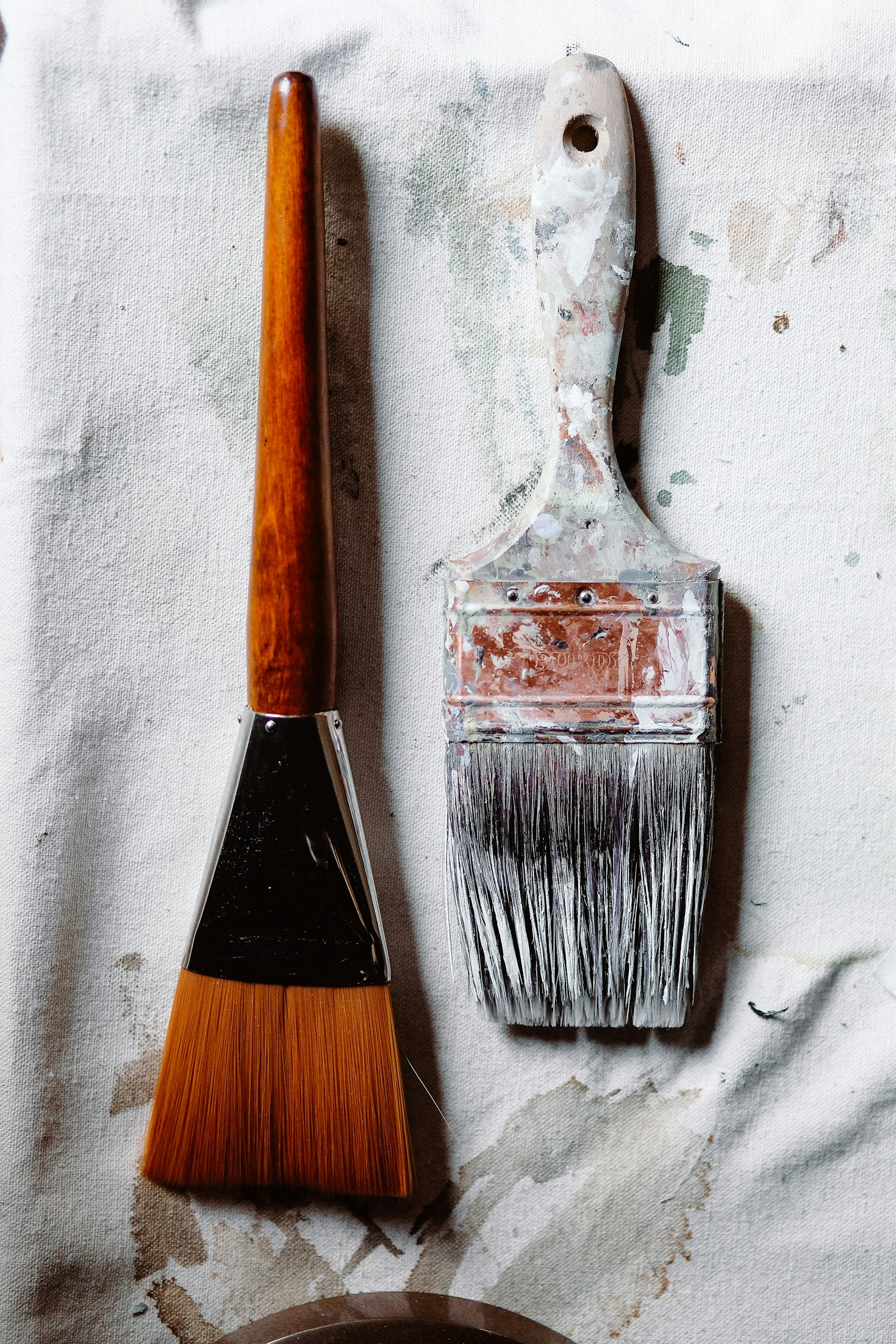 Two well used brushes lying on a paint spattered canvas drop cloth