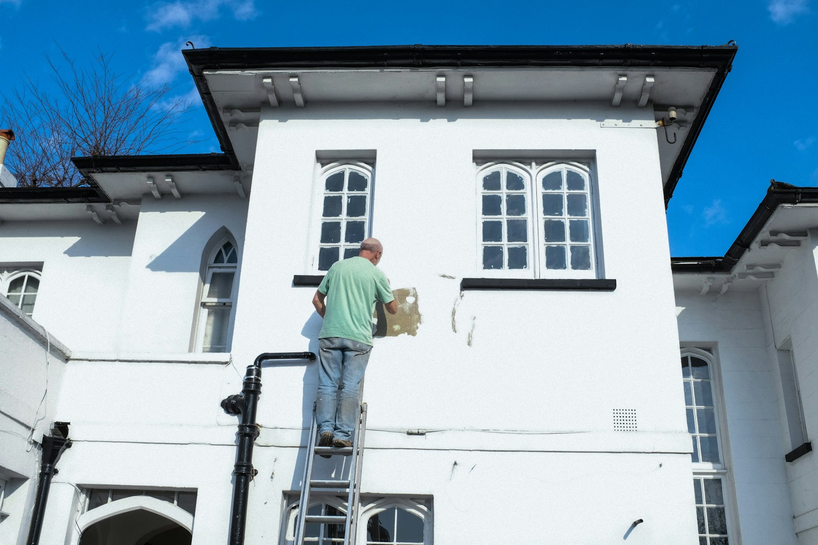 A worker on a ladder filling and smoothing a damaged patch of exterior render before repainting